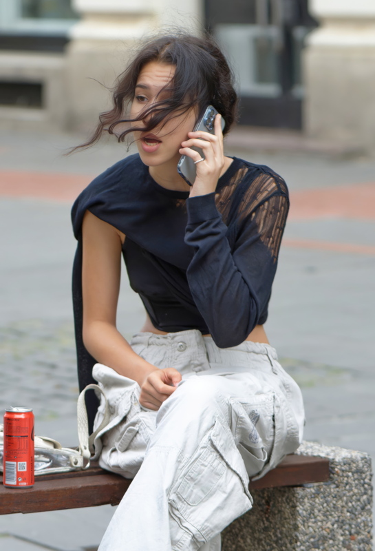 14 - A person wearing a layered black top paired with casual light-coloured utility cargo pants while talking on a smartphone